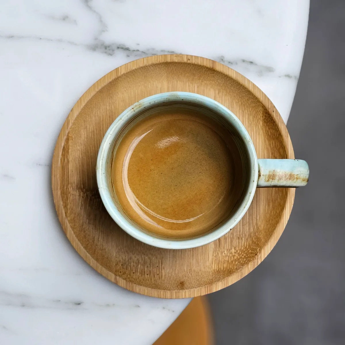 Overhead flat lay of a coffee cup on a worn wooden table, morning light falling across from the left. Warm, simple, editorial.