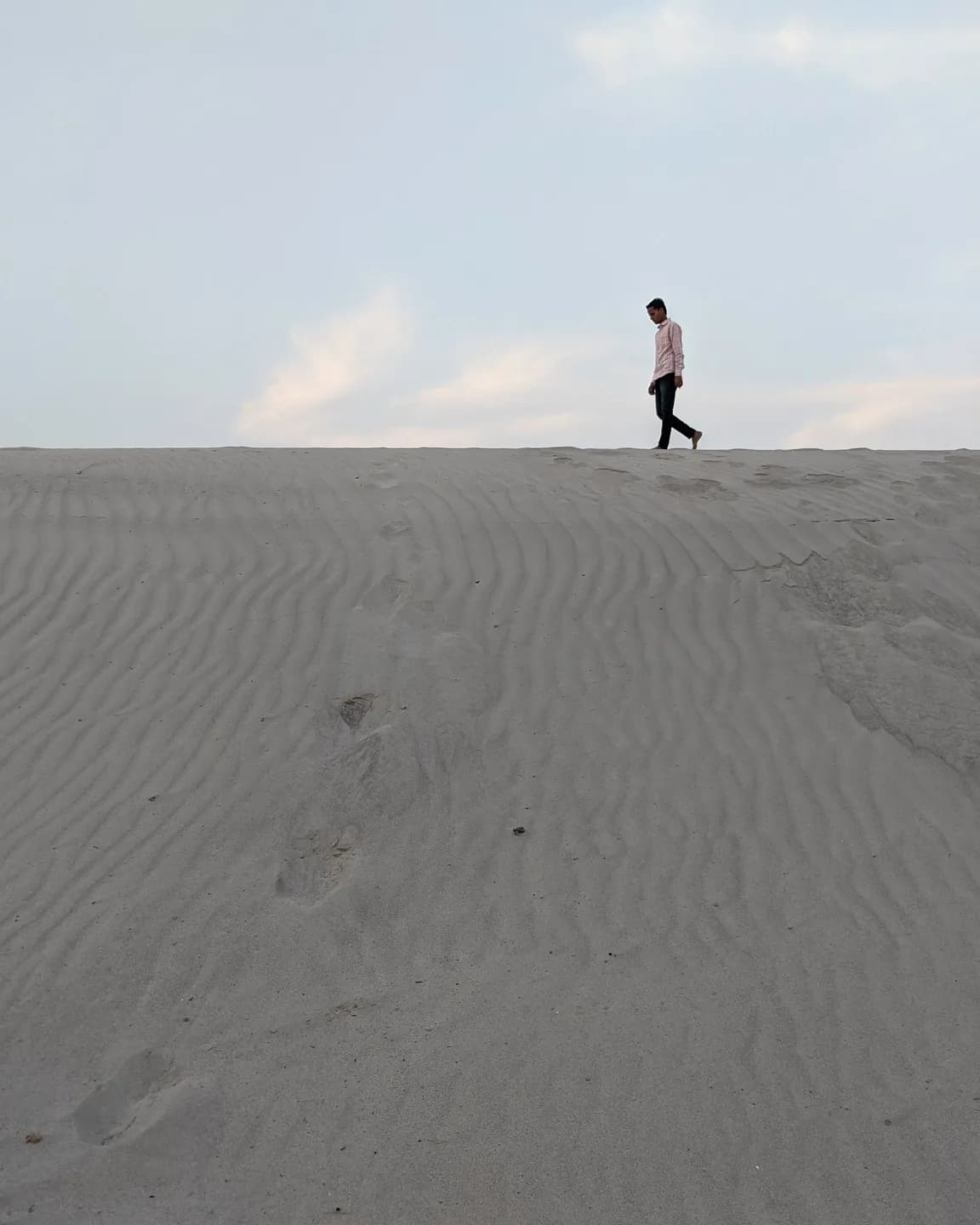 A lone figure crosses a vast dune field, tiny against the ridgeline. Late sun, long shadow, scale-driven and cinematic.
