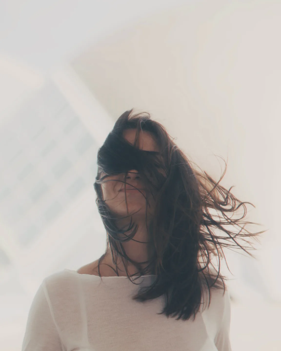 A woman outdoors with hair caught mid-movement, looking just past the lens. Overcast light, soft contrast, natural and unposed.