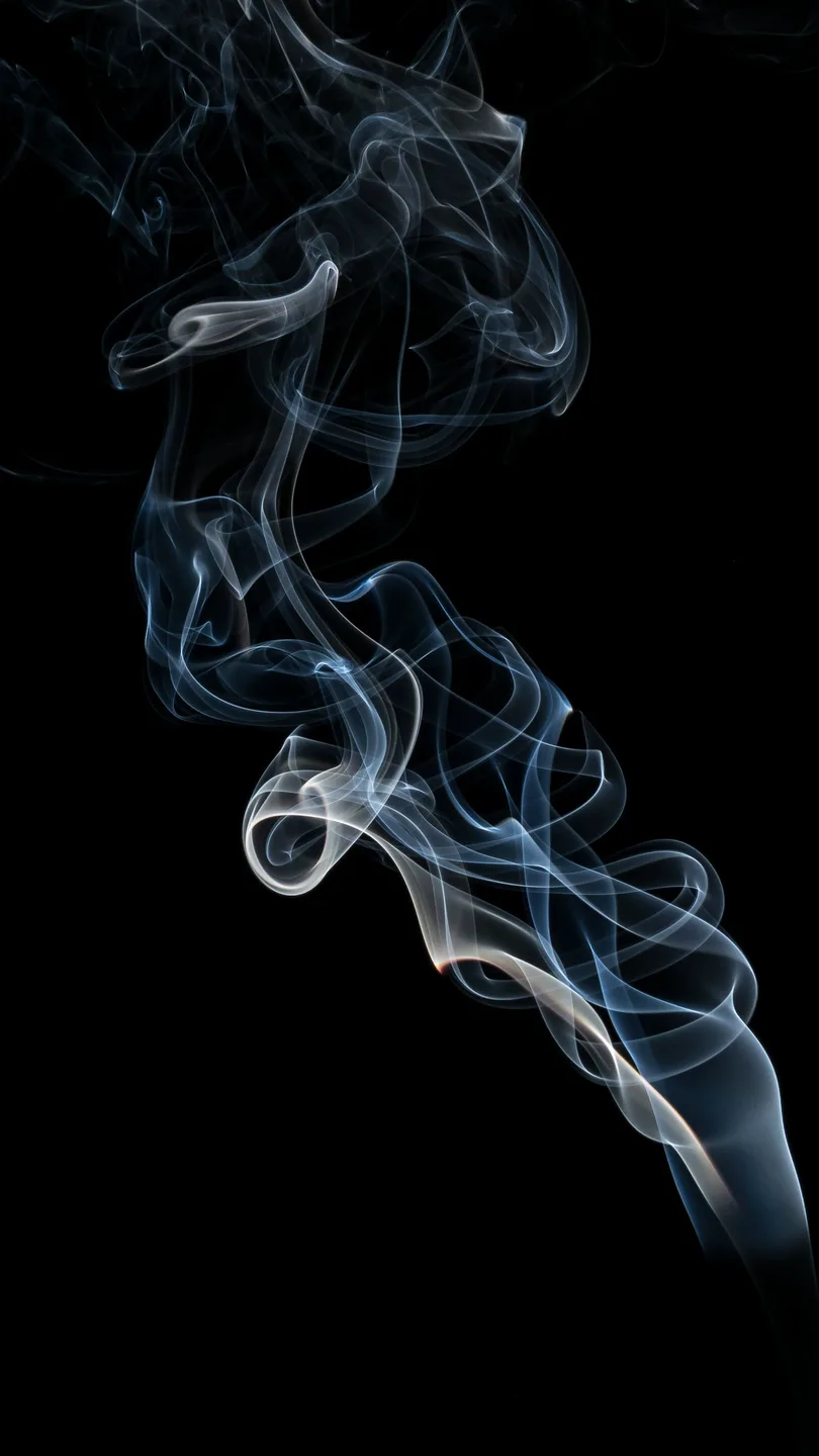 A single column of smoke rising and breaking apart against black. Side-lit, monochrome, sculptural.