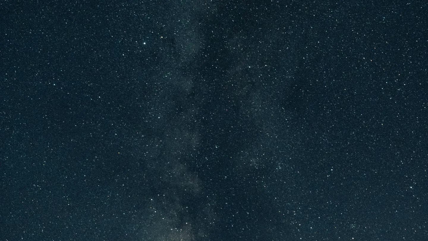 The Milky Way arcing over a dark horizon, stars dense from edge to edge. Long exposure, cold tones, vast and silent.