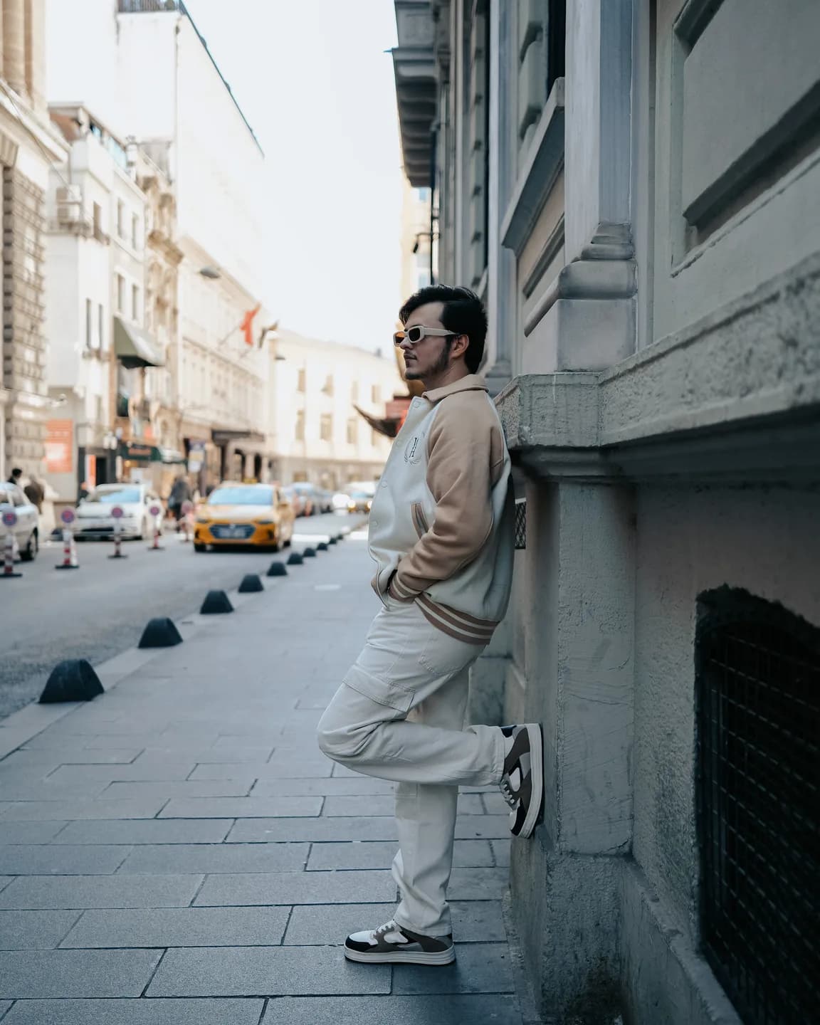 Full-length street style frame against a plain city wall, strong silhouette, confident stance. Flat overcast light, muted tones, editorial.