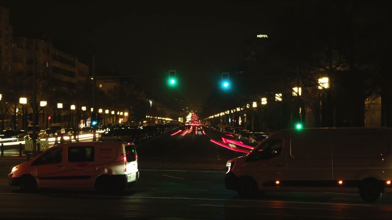 Traffic streams into light trails across a city intersection in timelapse, towers lit behind. High wide angle, saturated reds and ambers.