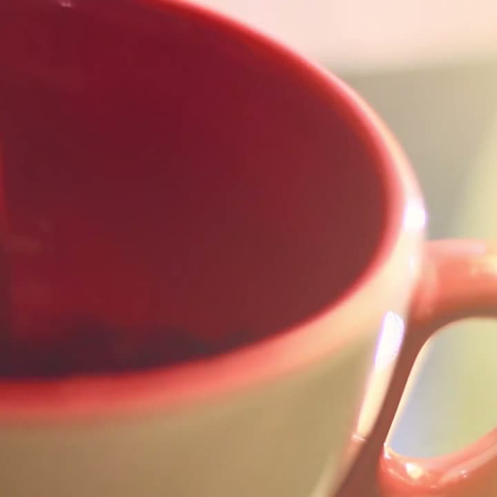 Coffee streams into a ceramic cup, crema swirling as it fills. Tight overhead macro, warm side light, rich browns against matte stone.