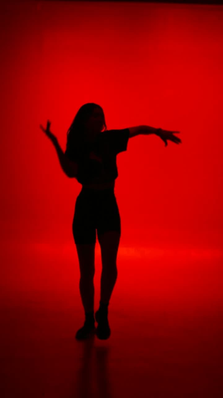 A dancer moving through a slow spin, body caught in a single hard light against darkness. Camera holds steady, motion blur trails the limbs. Dramatic and graphic.