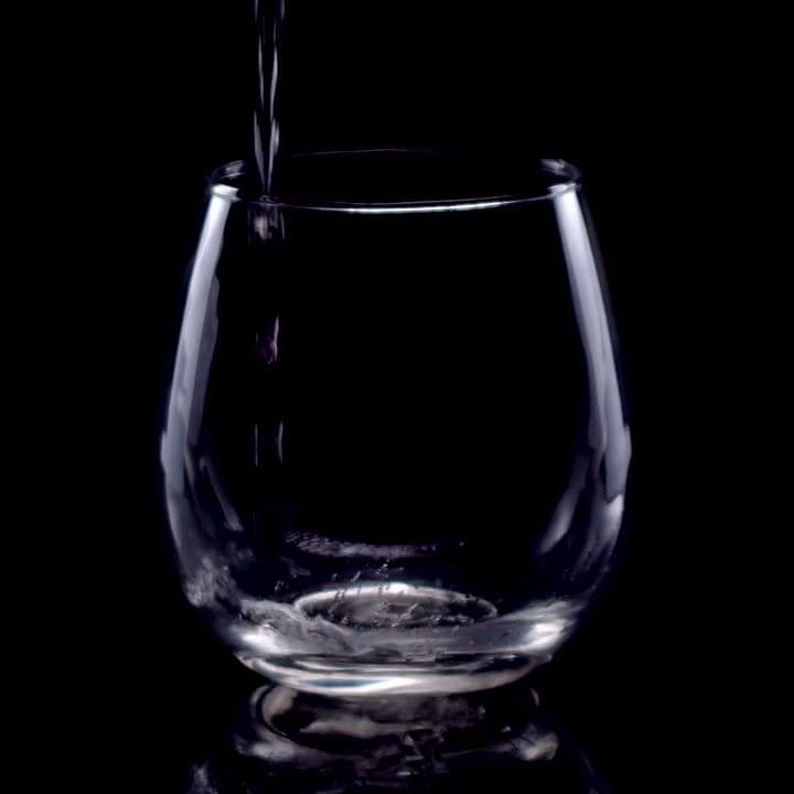 Liquid splashes up the inside of a glass in slow motion, droplets suspended mid-air. Hard backlight, crisp highlights, clean and graphic.