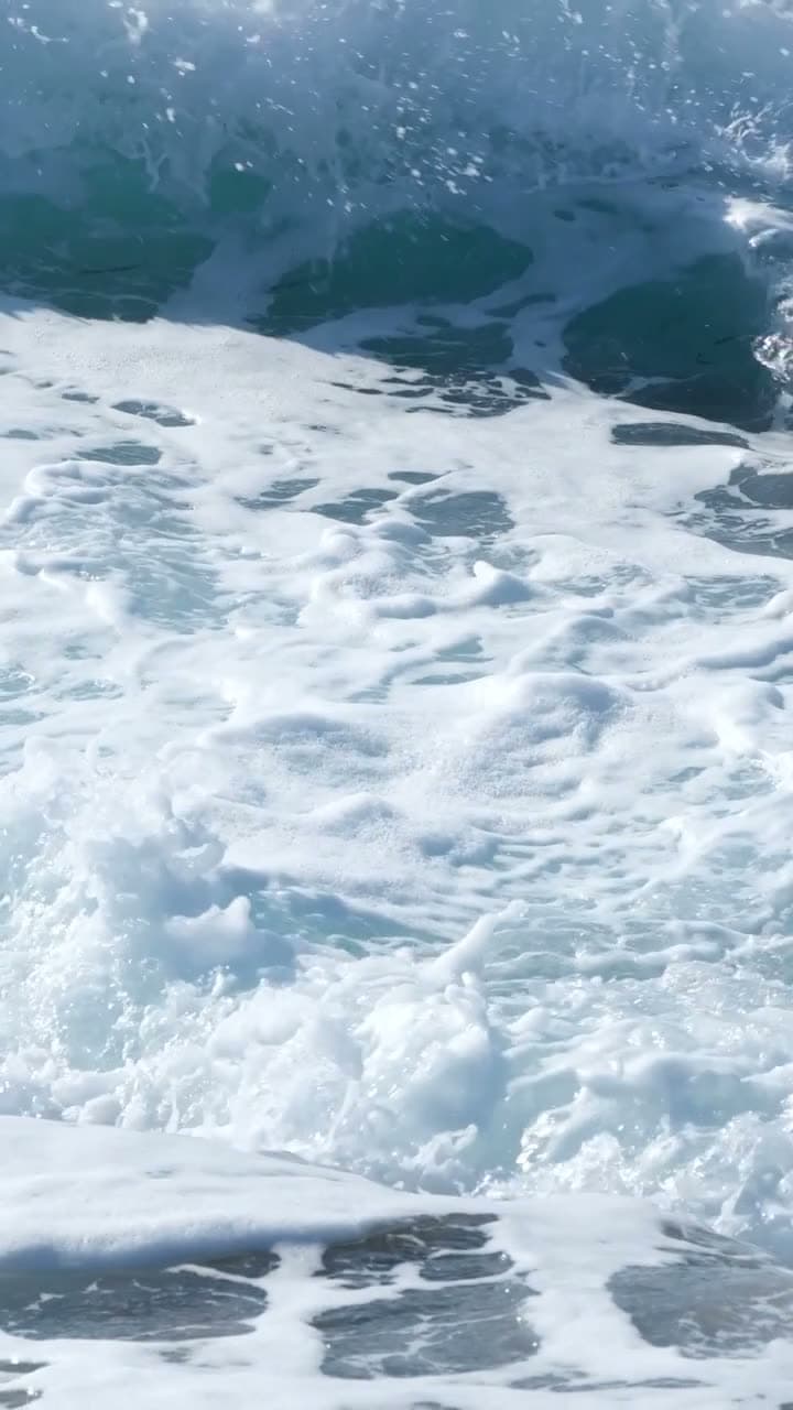 Ocean swell rolls and breaks, filmed from just above the waterline in slow motion. Foam spreads across deep blue-green. Weighty and meditative.