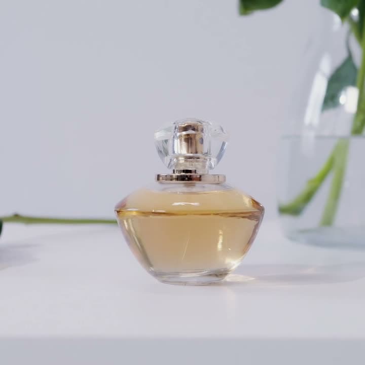 A glass bottle rotates slowly on a dark plinth, light raking across its facets. Studio lighting, deep shadow, premium and restrained.