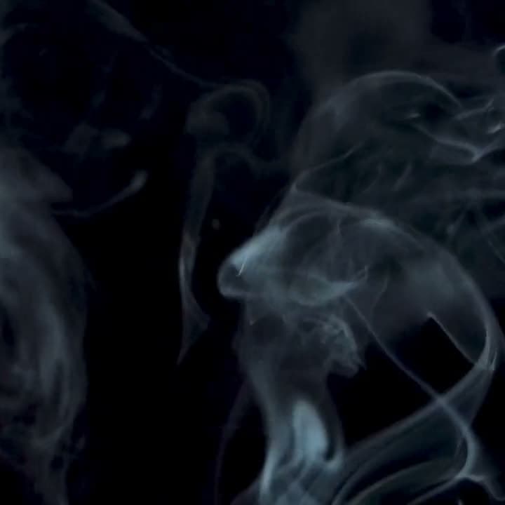 Smoke curls upward through a single beam of light against black. Slow, continuous motion, monochrome, textural and abstract.