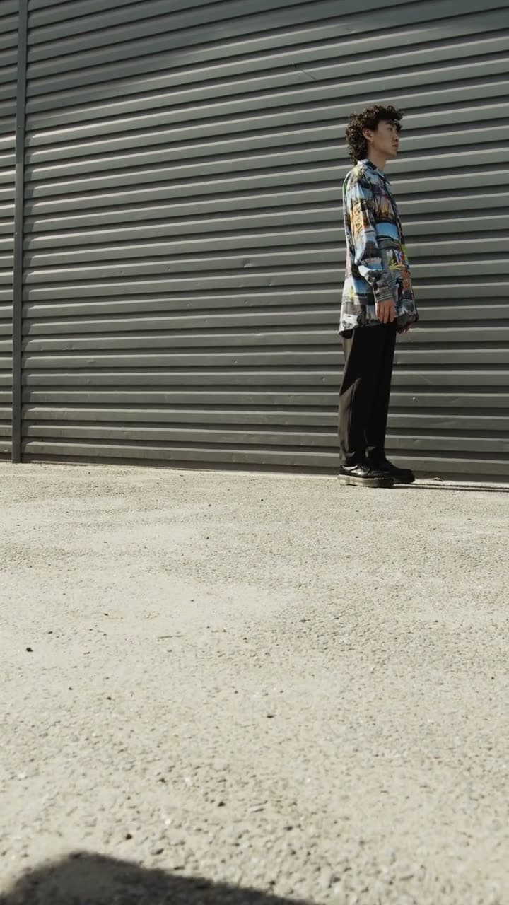 A person in a long coat walks toward camera down a city pavement, coat moving with each step. Overcast light, muted palette, editorial and confident.